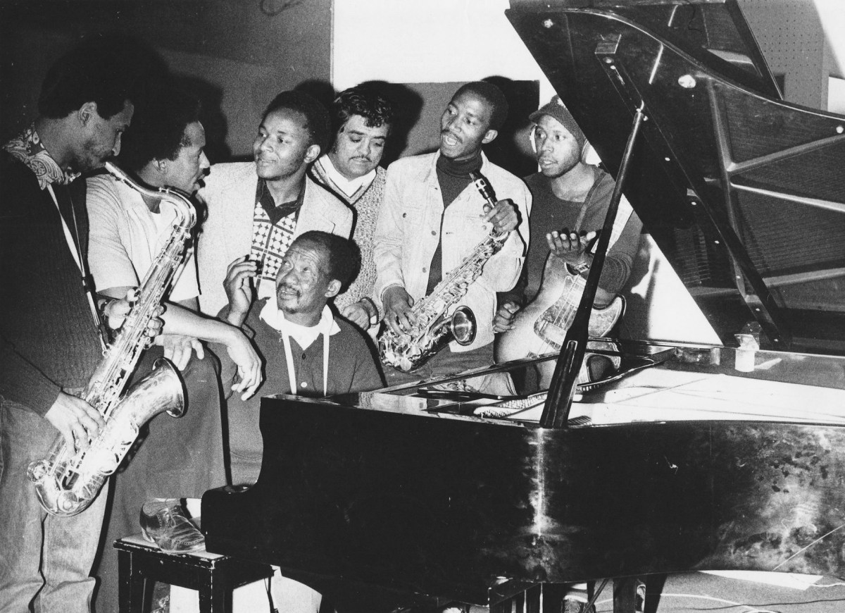 Kippie Moeketsi at piano with, from left, musicians Basil Coetzee, Pat Matshikiza, Selby Ntuli, producer Rashid Vally, Sipho Mabuse and Alec Khaoli. (Image courtesy As Shams Archive)