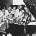 Kippie Moeketsi at piano with, from left, musicians Basil Coetzee, Pat Matshikiza, Selby Ntuli, producer Rashid Vally, Sipho Mabuse and Alec Khaoli. (Image courtesy As Shams Archive)
