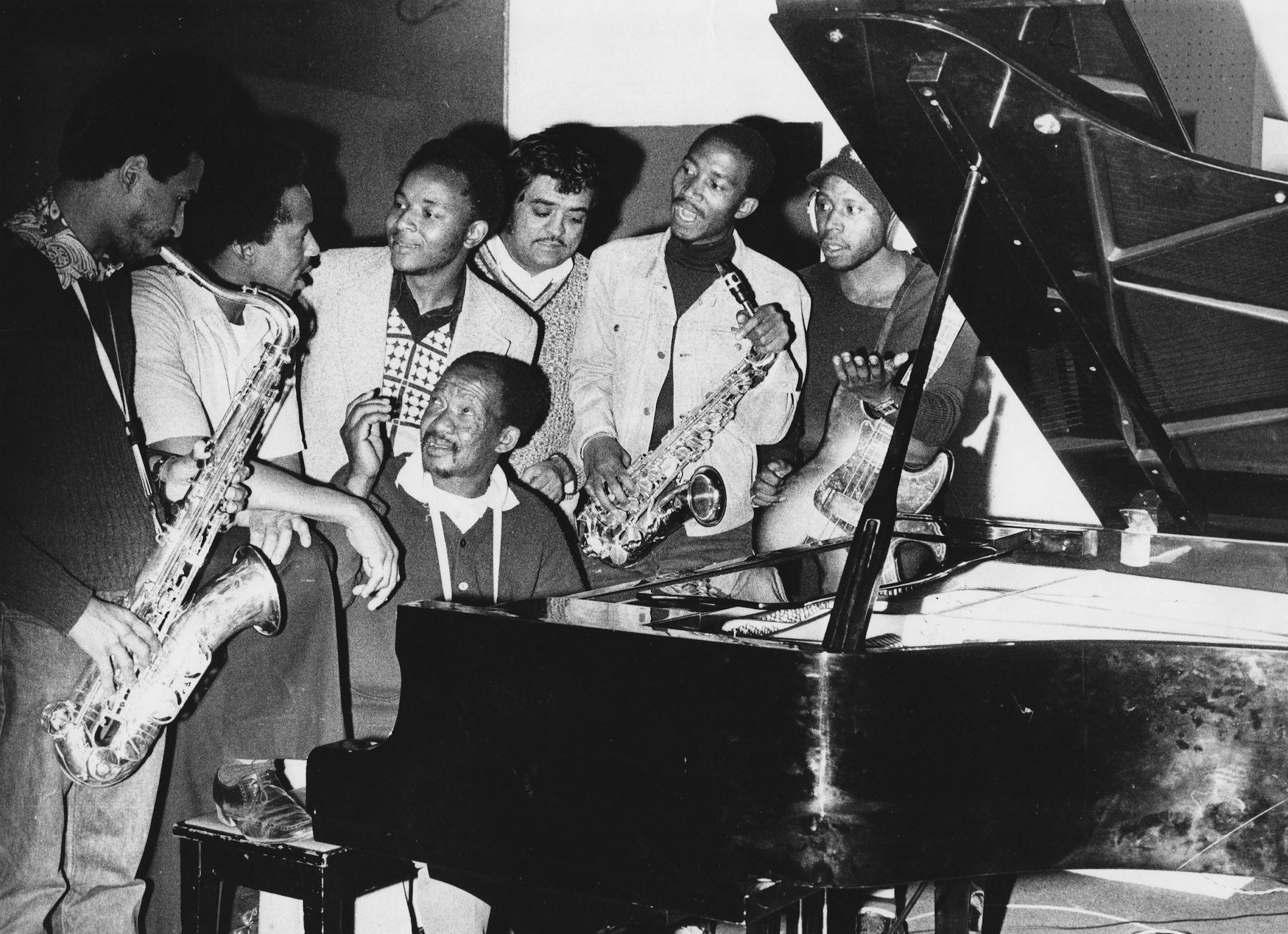 Kippie Moeketsi at piano with, from left, musicians Basil Coetzee, Pat Matshikiza, Selby Ntuli, producer Rashid Vally, Sipho Mabuse and Alec Khaoli. (Image courtesy As-Shams Archive)