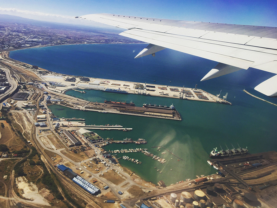 A plane passenger's view of Port Elizabeth harbour on the western curve of Algoa Bay in South Africa's Eastern Cape province. The port was established in 1825, five years after the first wave of British settlers into the Eastern Cape region in 1820. Today South African exports from the port include farming produce, manganese ore mined in the Northern Cape, and vehicles produced by the Eastern Cape's large automotive manufacturing industry. Port Elizabeth also handles overflow sea traffic from the larger ports at Durban and Cape Town.
